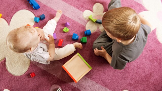 A boy aged three and a girl aged one are playing on the floor.View from above.